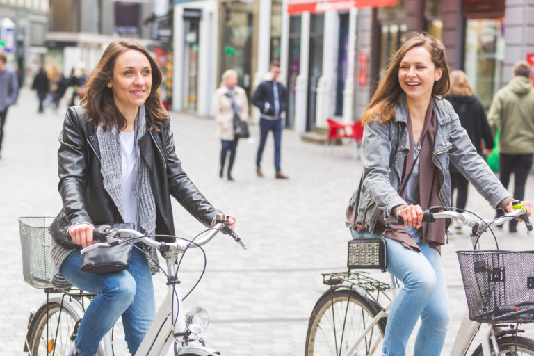 Two women going by bike in Copenhagen. They are in their twenties and they are wearing smart casual clothes. Bicycles are a typical mode of transport in Denmark.